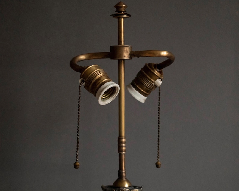 May include: A brass lamp base with two sockets and pull chains. The lamp base has a decorative design at the bottom.