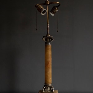 May include: A vintage brass and alabaster table lamp with a columnar base and two light sockets. The lamp has a decorative, ornate design.