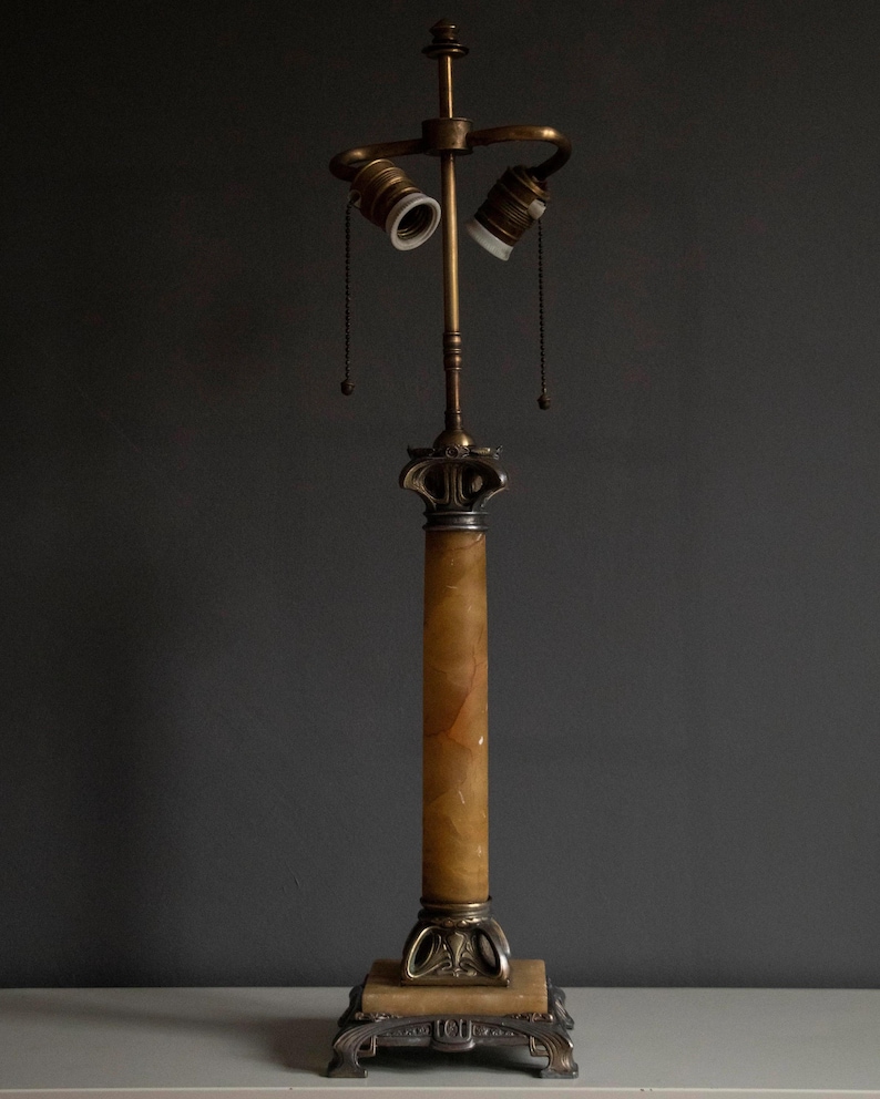 May include: A vintage brass and alabaster table lamp with a columnar base and two light sockets. The lamp has a decorative, ornate design.