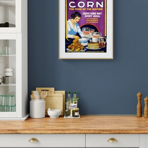 May include: A vintage-style poster in a light wood frame featuring the text CORN THE FOOD OF THE NATION SERVE SOME WAY EVERY MEAL APPETIZING NOURISHING ECONOMICAL UNITED STATES FOOD ADMINISTRATION with an illustration of a person preparing corn dishes.