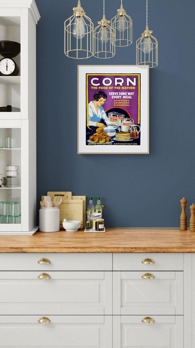 May include: A vintage-style poster in a light wood frame featuring the text CORN THE FOOD OF THE NATION SERVE SOME WAY EVERY MEAL APPETIZING NOURISHING ECONOMICAL UNITED STATES FOOD ADMINISTRATION with an illustration of a person preparing corn dishes.