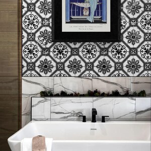 May include: A contemporary bathroom featuring a white bathtub, black taps, and a framed print. The wall is adorned with black and white patterned tiles, a marble border, and a small plant display. A white towel with a brown washcloth hangs on the tub.