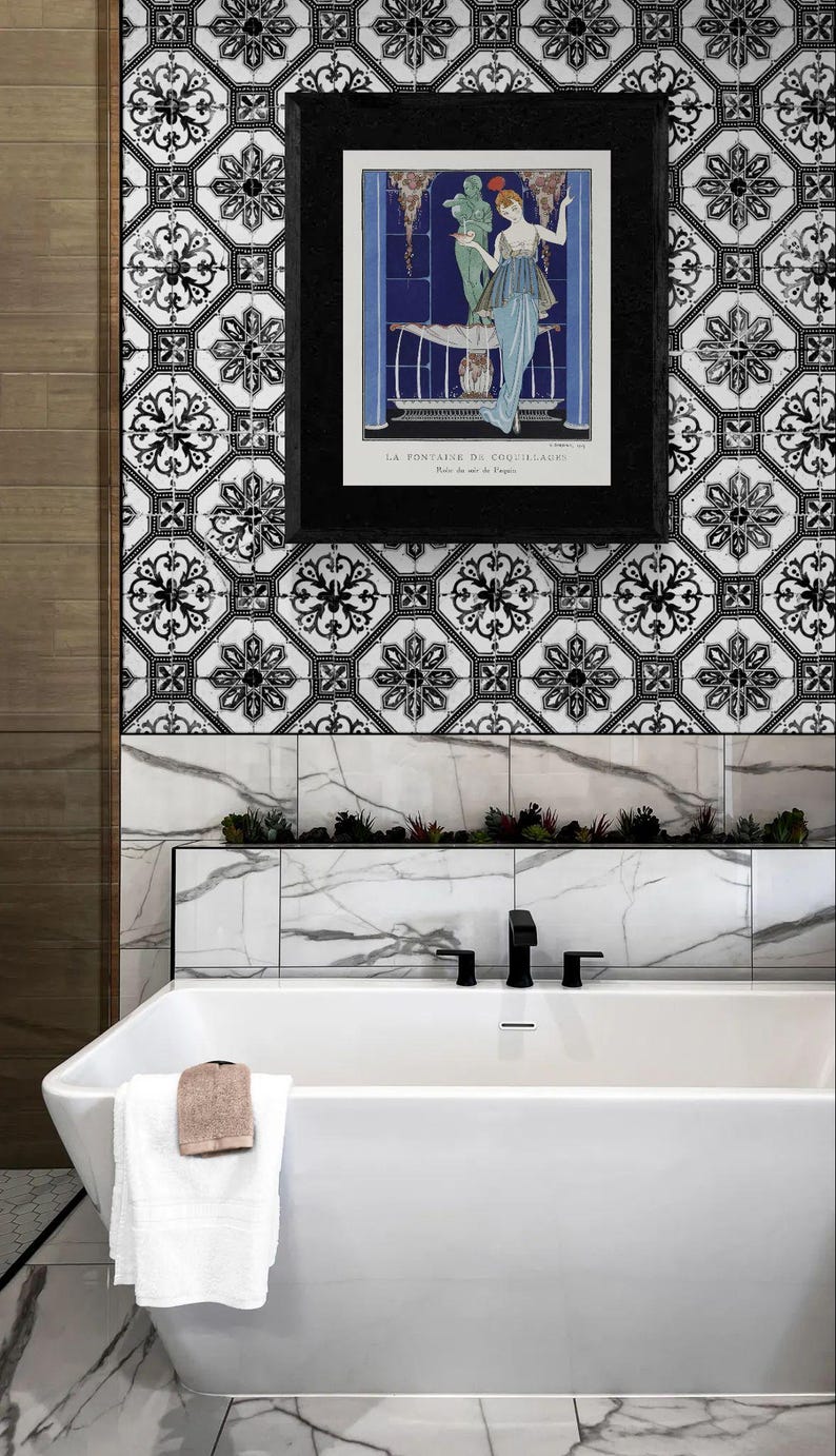 May include: A contemporary bathroom featuring a white bathtub, black taps, and a framed print. The wall is adorned with black and white patterned tiles, a marble border, and a small plant display. A white towel with a brown washcloth hangs on the tub.