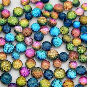 May include: Assortment of iridescent glass cabochons in various colors, including blue, green, purple, and gold. The cabochons are round and have a textured surface.