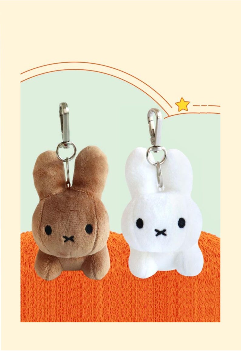 May include: Two plush bunny keychains, one brown and one white, each with a silver clip. The bunnies have black eyes and a black 'X' mouth. They are set against an orange and light green background.