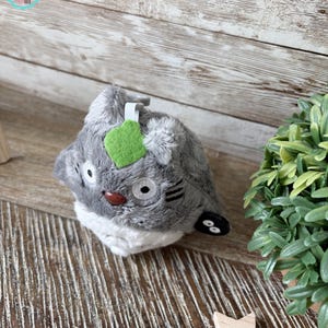 Puede incluir: Juguete de peluche gris y blanco con una hoja verde en la cabeza. El juguete tiene ojos negros y una nariz marr&oacute;n. Es un personaje de la pel&iacute;cula Mi vecino Totoro.
