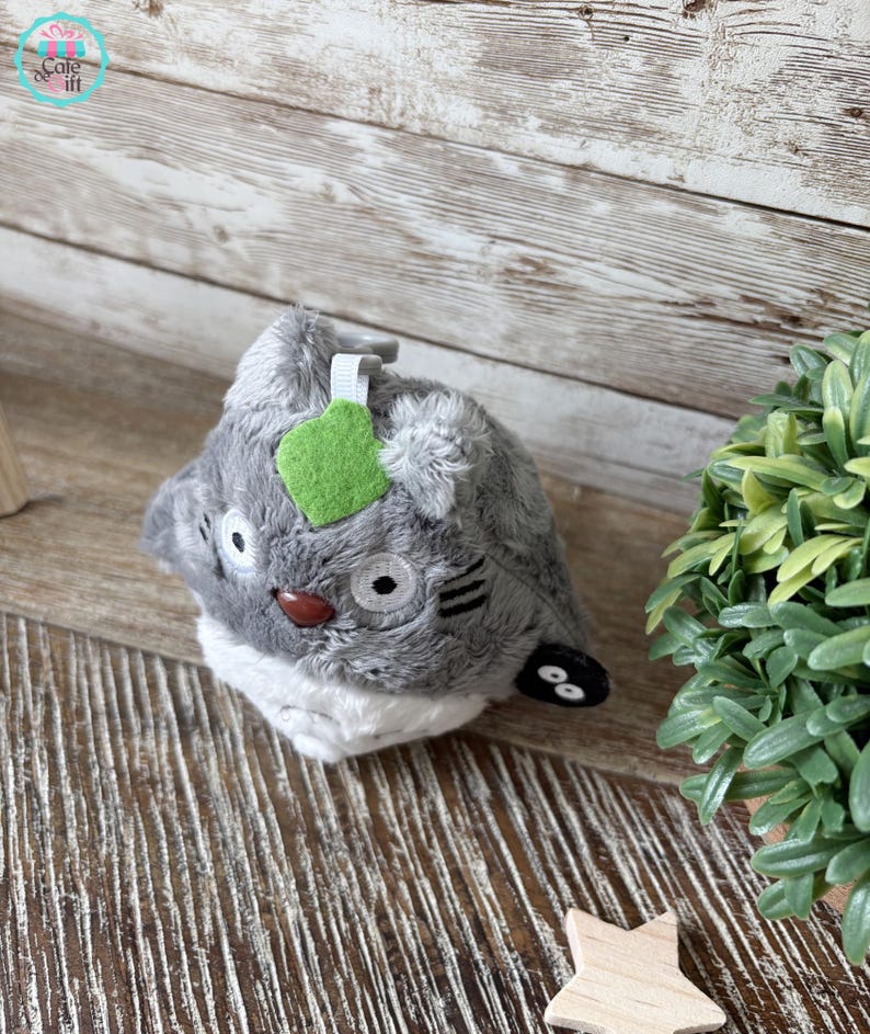 Puede incluir: Juguete de peluche gris y blanco con una hoja verde en la cabeza. El juguete tiene ojos negros y una nariz marr&oacute;n. Es un personaje de la pel&iacute;cula Mi vecino Totoro.