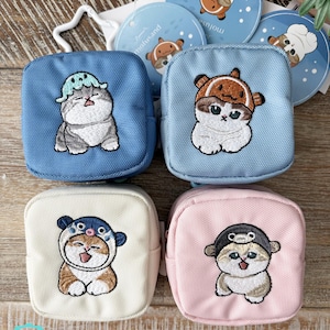 May include: Four small, square pouches in blue, light blue, cream, and pink, each embroidered with a cartoon cat wearing a hat. The pouches are zippered and have a small loop. Round stickers with a cat design are also visible.