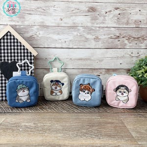 May include: Four small, square pouches in blue, white, light blue, and pink, each with a different embroidered cat design. The pouches have a zipper closure and a star-shaped or circular clip. The background is a wooden surface.