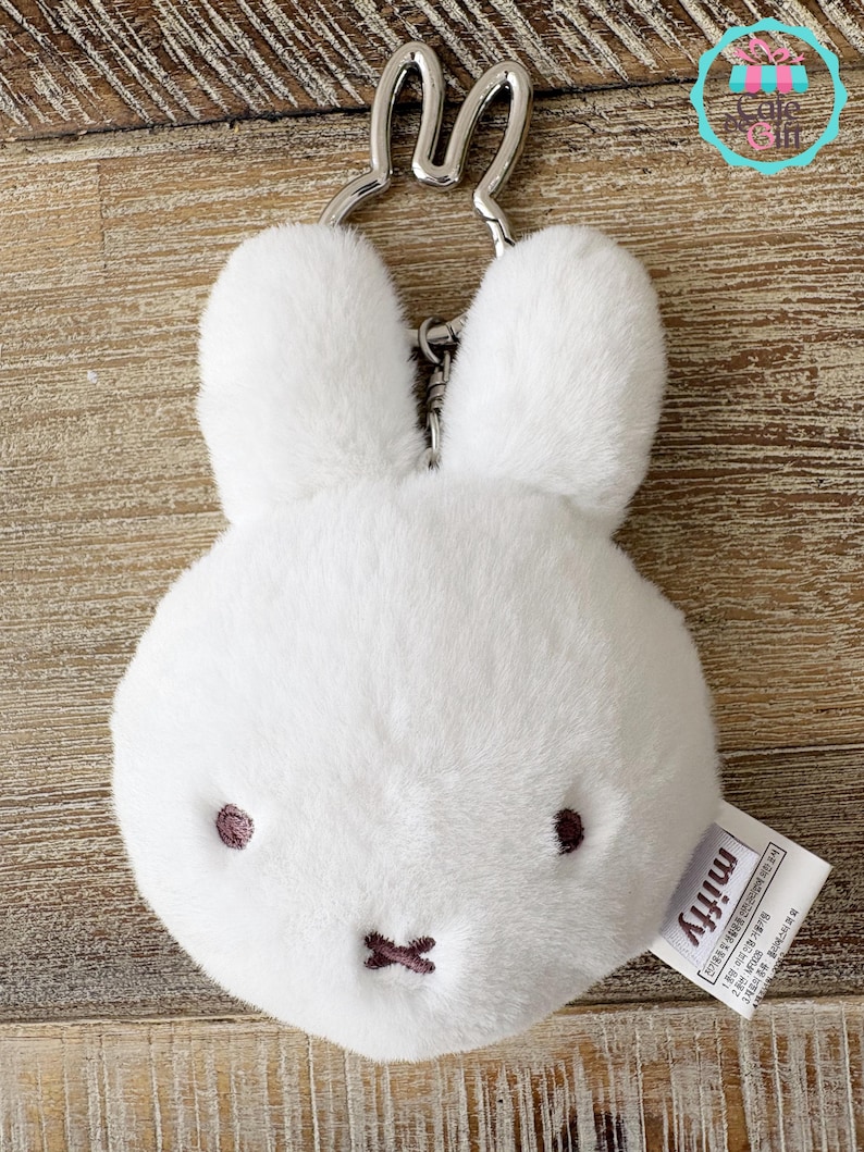 May include: A white plush bunny keychain with a silver-colored metal keyring. The bunny has embroidered dark brown eyes and a stitched mouth. The tag reads "miffy".