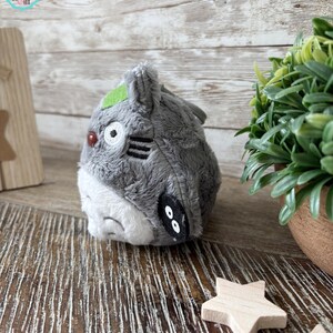 Puede incluir: Un juguete de peluche gris con la barriga blanca y ojos negros. El juguete tiene una oreja verde y un patr&oacute;n de rayas blancas y negras en la espalda. El juguete est&aacute; sentado sobre una superficie de madera.