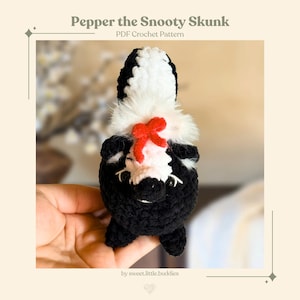 May include: A handmade crochet skunk toy, primarily black and white, with a fluffy white chest and a red bow. The skunk has small black eyes and is held in a hand. The text "Pepper the Snooty Skunk" and "PDF Crochet Pattern" are visible.