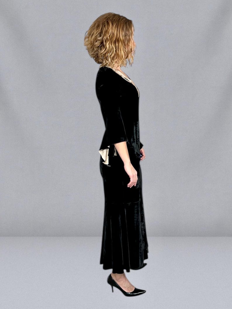 Puede incluir: Un vestido de terciopelo negro con escote en V y mangas tres cuartos. El vestido tiene un corpi&ntilde;o ajustado y una falda acampanada, y se combina con tacones altos negros. El vestido tiene un ribete color crema.