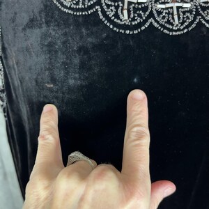 May include: Close-up of a black velvet garment with ornate beaded embellishments. The trim features a repeating pattern of white and silver beads. The garment's fabric appears soft and luxurious, with a slight sheen. The image shows a portion of the garment.