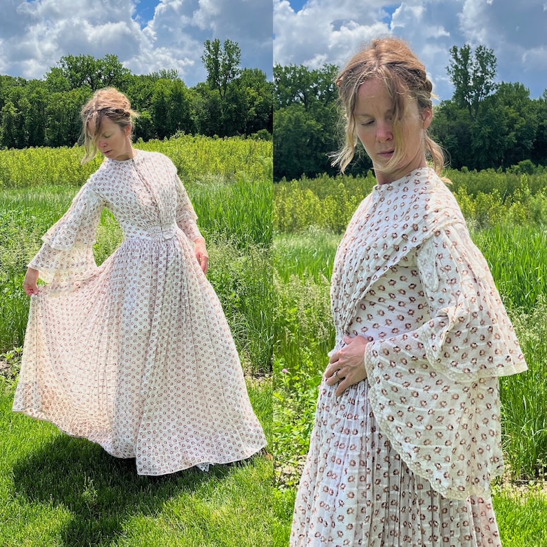 May include: A white dress with a floral pattern and ruffled sleeves. The dress is pleated and has a fitted bodice. The model is wearing the dress in a field of green grass.