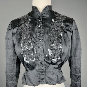 May include: A black satin blouse with a high collar and long sleeves. The blouse features a decorative design of sequins and beads on the front.