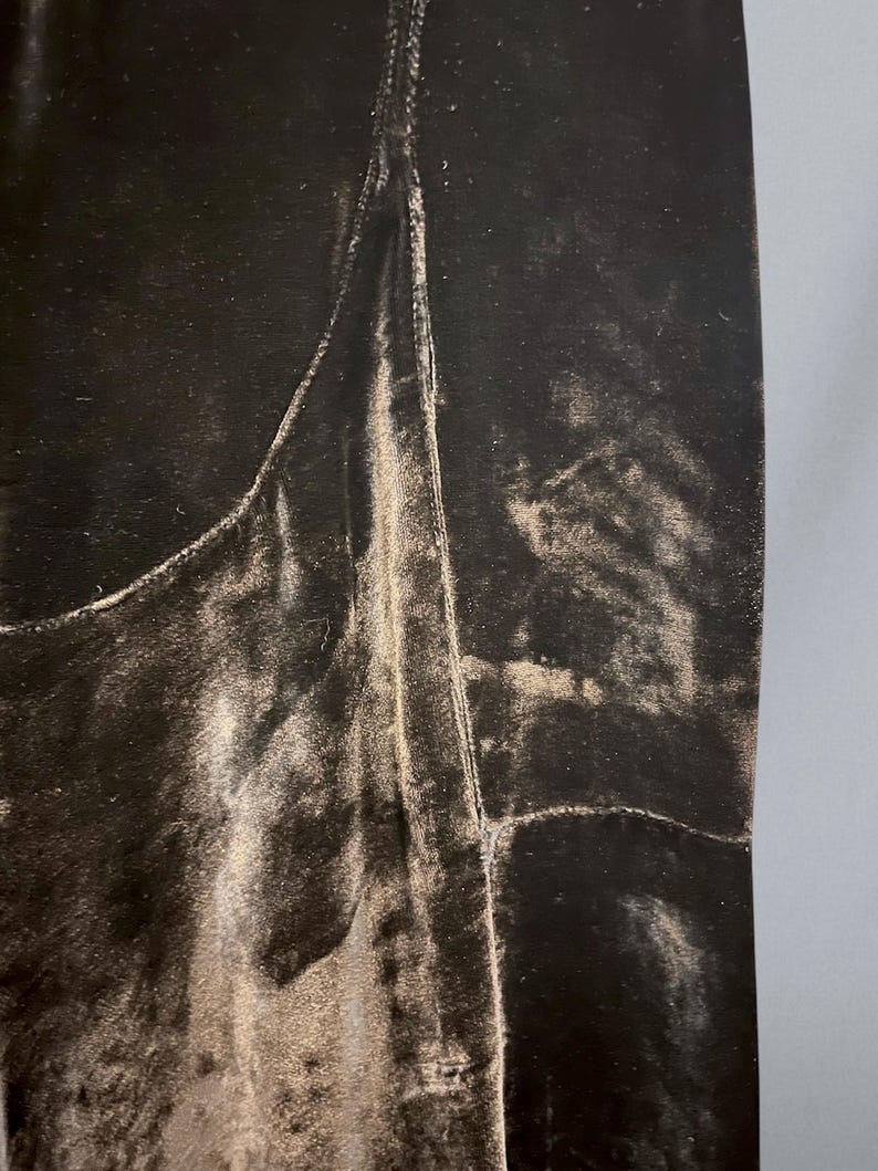 Puede incluir: Primer plano de una tela de terciopelo marr&oacute;n oscuro con un brillo sutil. La tela tiene un aspecto suave y texturizado con pliegues y arrugas visibles. La imagen resalta la textura lujosa y el color intenso del material.