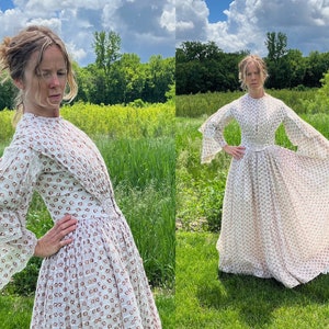 May include: A white dress with a floral pattern and long sleeves. The dress has a fitted bodice and a full skirt. The model is standing in a field of grass.
