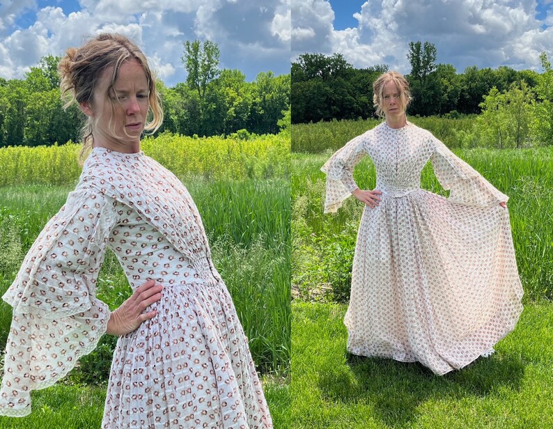 May include: A white dress with a floral pattern and long sleeves. The dress has a fitted bodice and a full skirt. The model is standing in a field of grass.
