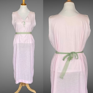 May include: A pale pink sleeveless dress with a green ribbon tied at the waist. The dress has a V-neck and a delicate embroidered design on the front.