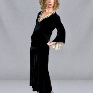 Puede incluir: Un vestido largo de terciopelo negro con escote en V y mangas acampanadas. El escote est&aacute; adornado con una tela color crema con detalles dorados. El vestido se combina con tacones negros.
