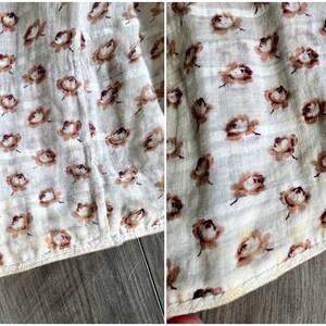 May include: Close-up of a white fabric with a brown floral pattern. The fabric has a subtle striped texture and is sewn with a brown thread.
