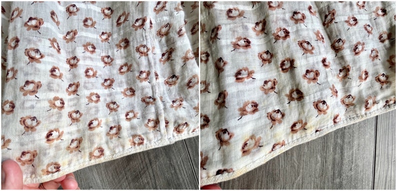 May include: Close-up of a white fabric with a brown floral pattern. The fabric has a subtle striped texture and is sewn with a brown thread.