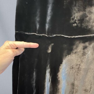 Puede incluir: Primer plano de una tela de terciopelo gris oscuro. La tela tiene un aspecto suave y brillante con sutiles variaciones de tono. La textura parece suave y fluida, con una costura visible. La tela est&aacute; drapeada, creando pliegues y sombras suaves.