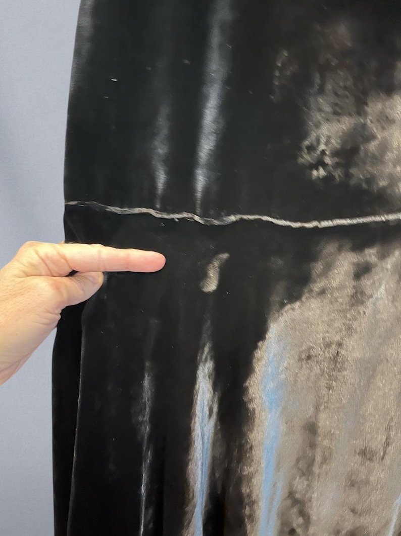 Puede incluir: Primer plano de una tela de terciopelo gris oscuro. La tela tiene un aspecto suave y brillante con sutiles variaciones de tono. La textura parece suave y fluida, con una costura visible. La tela est&aacute; drapeada, creando pliegues y sombras suaves.