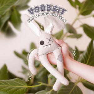 Peut inclure: Une peluche lapin en tissu gris clair avec de longues oreilles, un œil en bouton noir, un œil cousu en forme de croix, deux dents carrées blanches et une pièce gris foncé sur une jambe. Le texte "VOOBBIT PDF SEWING PATTERN" est écrit en blanc.