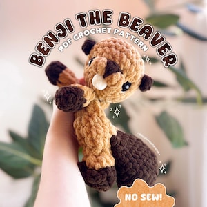 May include: A crocheted Benji the Beaver plushie in shades of brown, tan, and dark brown. The plushie has a round head, small ears, and a distinctive tail. The text "BENJI THE BEAVER PDF CROCHET PATTERN" is arched above the beaver.