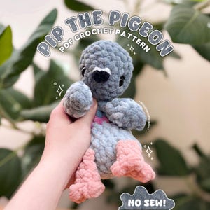 Könnte beinhalten: Ein handgefertigtes gehäkeltes Taubenspielzeug in Grau und Rosa. Der Plüschvogel hat einen schwarzen Schnabel und ist mit "Pip the Pigeon PDF Crochet Pattern" beschriftet. Der Text "No Sew!" ist ebenfalls sichtbar. Das Spielzeug wird in einer Hand gehalten.
