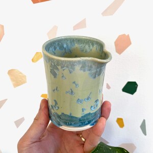 Peut inclure: Pichet en céramique fait à la main avec un glaçage unique. Le pichet présente une base vert clair avec des accents bleus et une texture cristalline. Le bord et la base sont bleu foncé. Le pichet a un petit bec verseur.