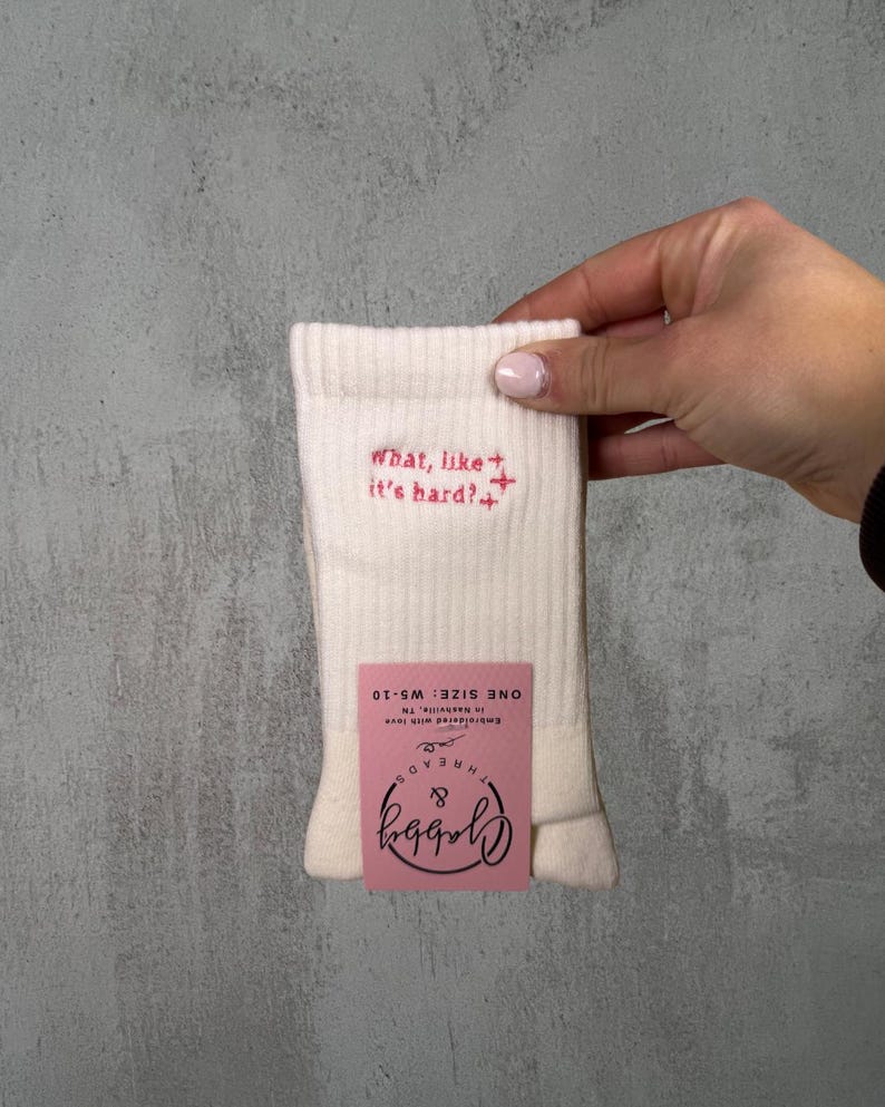 a pair of white socks with the text "what like its hard" embroidered on it against a white background