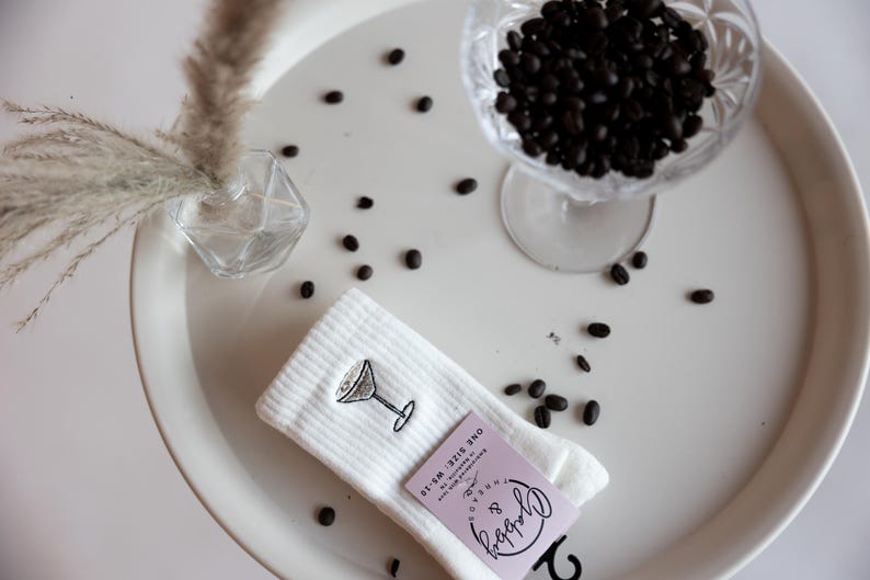 a pair of white socks with an embroidered espresso martini sits on a table with espresso beans