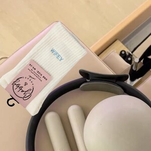 a pair of white grip socks with the word "wifey" embroidered on them sits next to workout equipment on a reformer