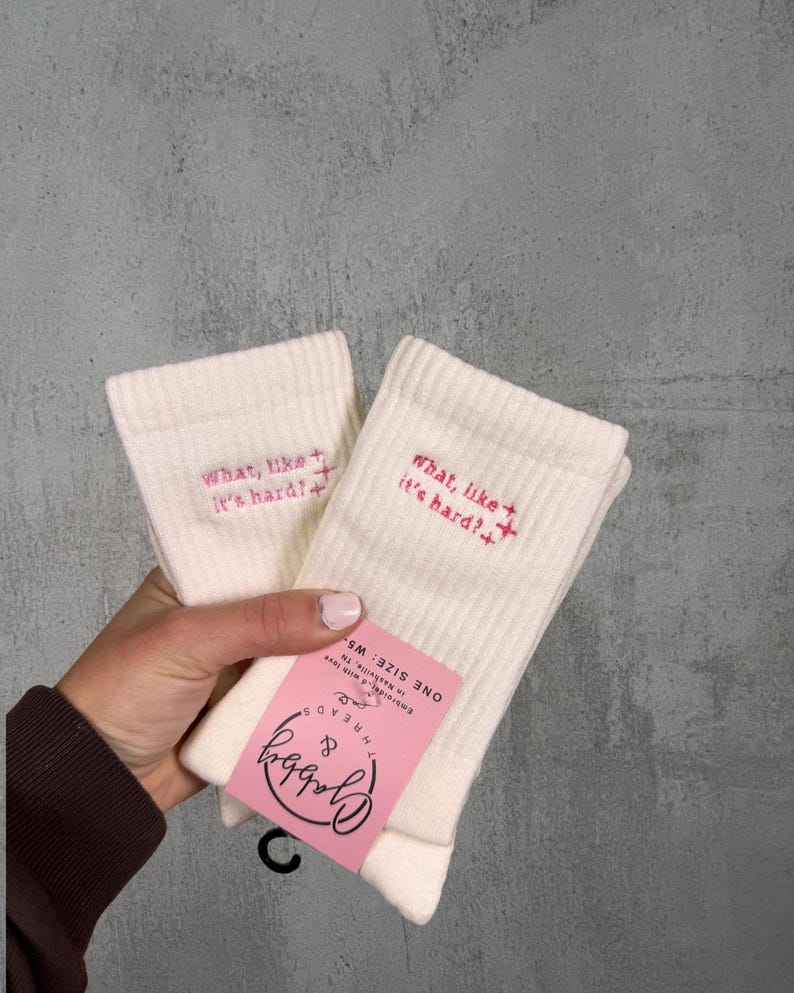 two pairs of white socks with the text "what like its hard" embroidered on them against a white background