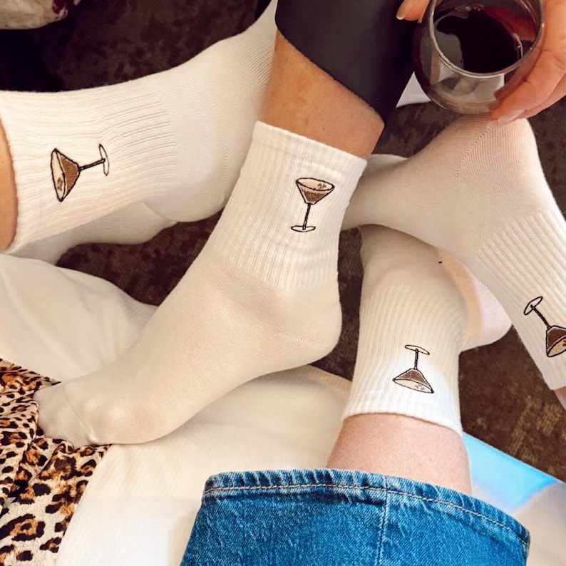 White socks with embroidered espresso martini designs worn by a person sitting on a couch.