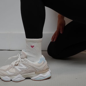Person wearing white sneakers and a sock with a heart design on a light-colored floor.