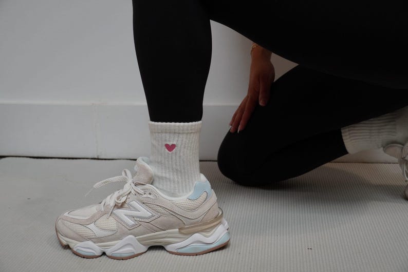 Person wearing white sneakers and a sock with a heart design on a light-colored floor.