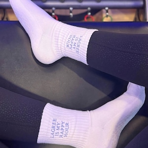a pair of white grip socks are on someone's feet that say "lagree is my happy hour" while sitting on a pilates reformer
