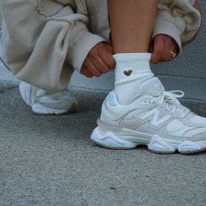 Person wearing white sneakers and a sock with a heart design sitting on concrete floor