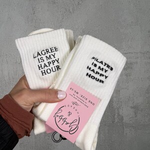 two pairs of white grip socks with the words "Lagree is my happy hour" and "pilates is my happy hour" embroidered on them