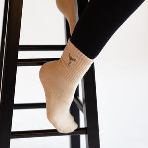 Person wearing beige socks with an embroidered espresso martini n a black stool against a white background