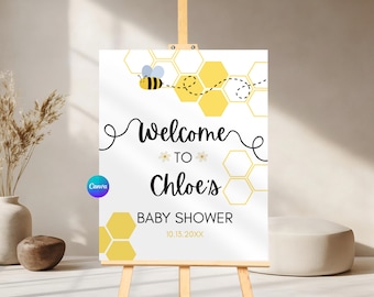 May include: A white baby shower welcome sign on an easel. The sign features a cartoon bee, honeycomb graphics, and the text "Welcome to Chloe's Baby Shower" with a date. The Canva logo is visible in the lower left corner.