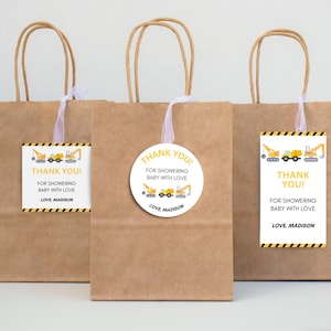 May include: Three brown paper gift bags with handles, each with a tag or sticker. The tags and sticker feature construction vehicles and the text "THANK YOU!" and "FOR SHOWERING BABY WITH LOVE, LOVE, MADISON."