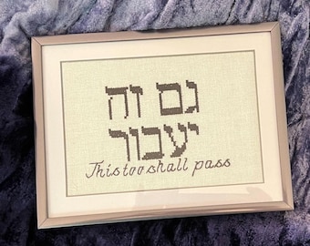 May include: A framed cross-stitch with Hebrew text and the phrase "This too shall pass".