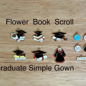 K&ouml;nnte beinhalten: Eine Sammlung von Charms zum Thema Abschluss, darunter Doktorh&uuml;te, Schriftrollen, B&uuml;cher und eine Robe. Einige Charms haben die Buchstaben T, C, M und L. Der Text "Flower Book Scroll" und "Graduate Simple Gown" ist ebenfalls sichtbar.