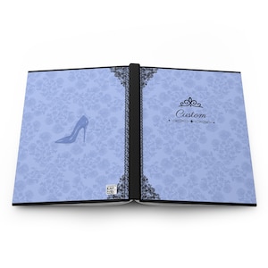 May include: A light blue open notebook with a black spine and black lace-style borders. The cover features a subtle floral pattern, a silhouette of a high-heeled shoe on the left, and the word Custom with a decorative flourish on the right.