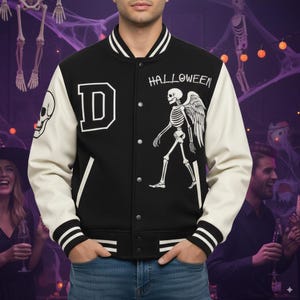 Könnte beinhalten: Schwarz-cremefarbene Halloween-Collegejacke mit Skelettgrafik und dem Wort "HALLOWEEN". Die Jacke hat ein großes weißes "D" auf der Brust und einen Totenkopf auf dem Ärmel. Die Jacke hat eine Knopfleiste und gestreifte Bündchen.